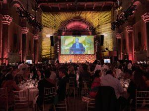 Big screen glows gold in a gorgeous event space filled with people